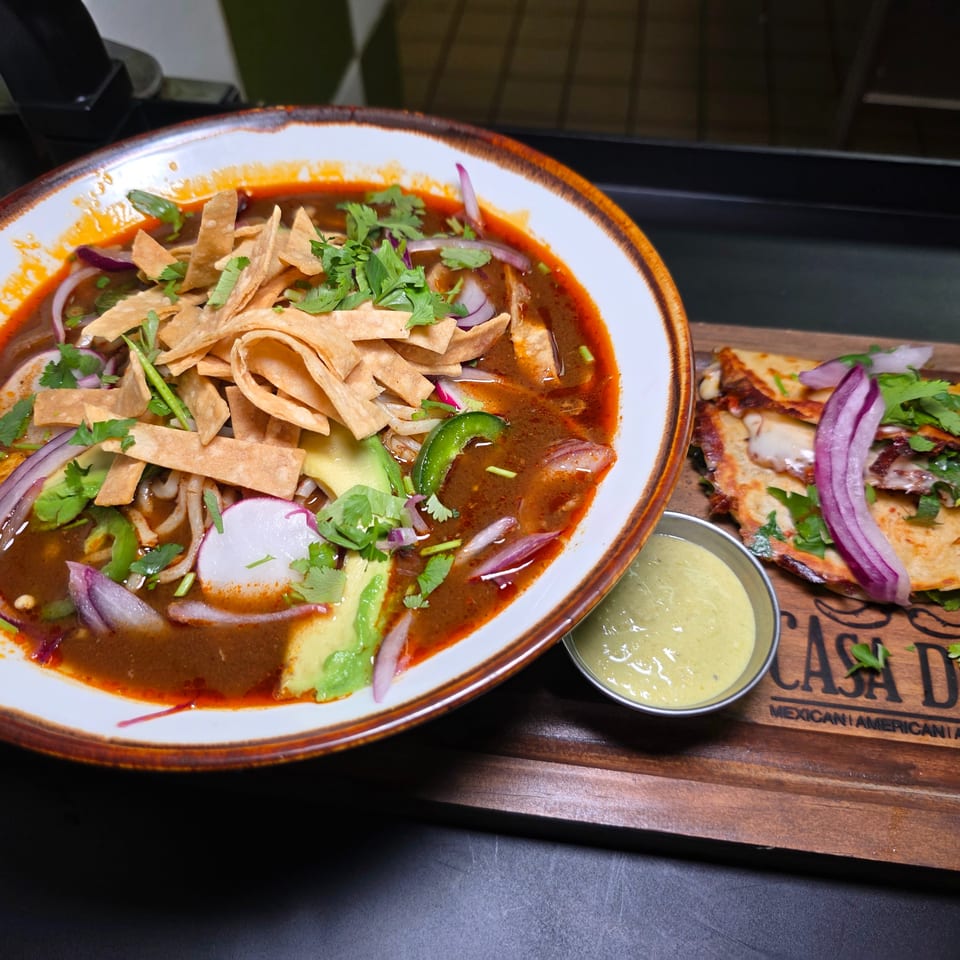 Mexican restaurant meal featuring spicy tortilla soup with avocado, cilantro, onions, and tortilla strips alongside a quesadilla and creamy dipping sauce.
