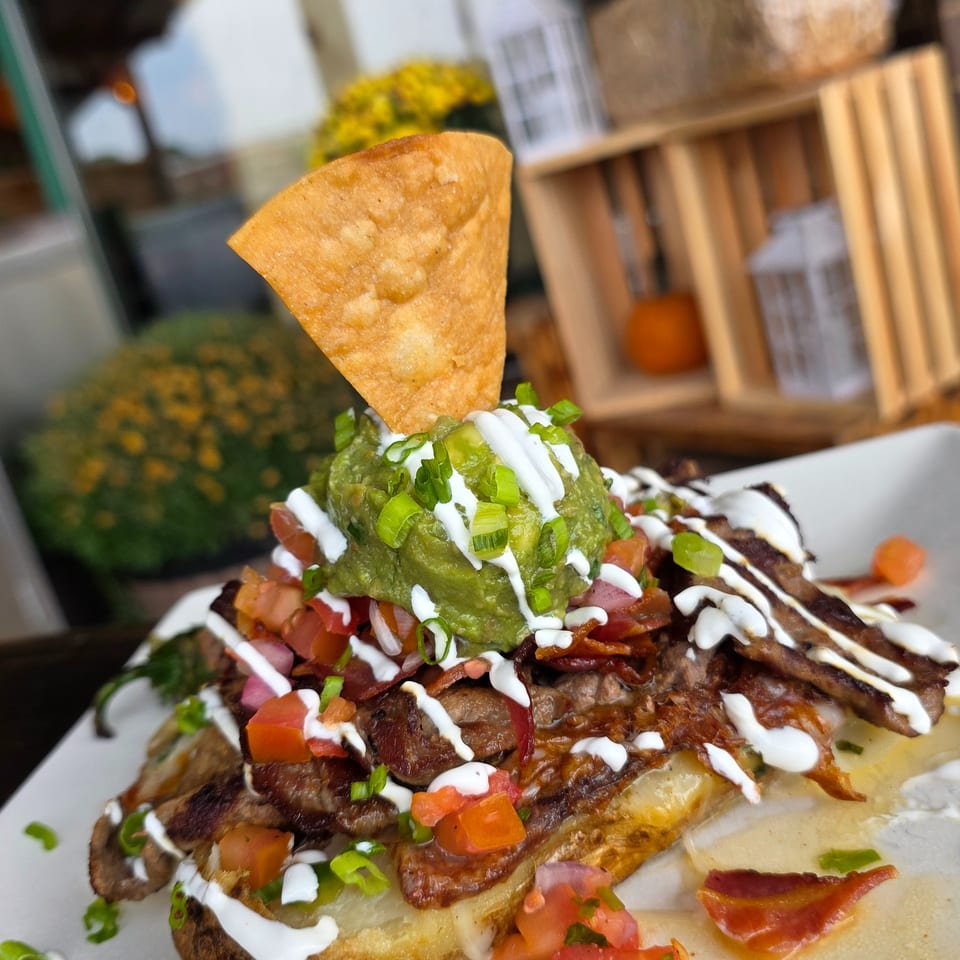 Loaded baked potato topped with guacamole, sour cream, bacon, diced tomatoes, scallions, and a crisp tortilla chip.
